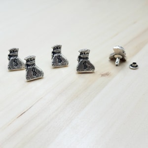 May include: Four silver-toned money bag studs with a dollar sign on each bag. The studs are on a light wood surface. There are two additional studs, one with a post and one with a flat back.