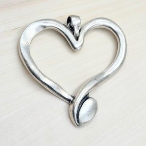 May include: A silver-toned open heart pendant with a smooth, curved design. The pendant has a simple, elegant style.