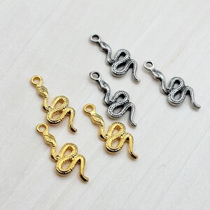 Puede incluir: Cinco encantos de serpiente de oro y plata. Los encantos tienen la forma de una serpiente enroscada con un bucle en la parte superior para sujetar a un collar o pulsera.