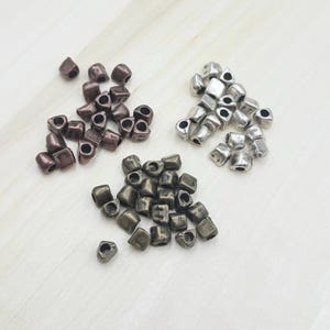 May include: Three piles of metal beads in different colours: copper, bronze, and silver. The beads are triangular in shape with a hole in the centre.