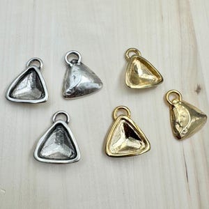 May include: Six triangle-shaped metal pendant charms with a beveled edge. Three charms are silver and three are gold.