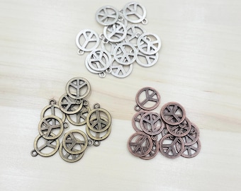 Puede incluir: Una colección de dijes con forma de signo de paz en tonos plateado, dorado y cobre. Los dijes son todos del mismo tamaño y forma, y tienen un agujero en la parte superior para sujetarlos a un collar o pulsera.