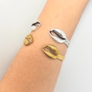 May include: A silver and gold bracelet with a shell design. The bracelet is adjustable and has a textured finish.