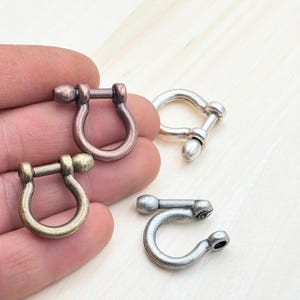 May include: Three metal D-ring clasps in different finishes: antique brass, copper, and silver. The D-rings are about 1 inch in diameter.