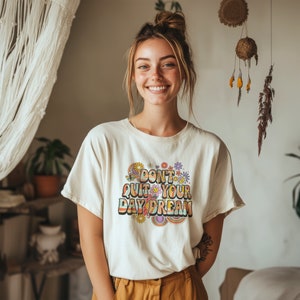 May include: A white t-shirt with a colorful graphic that says "Don't Quit Your Daydream". The graphic features flowers, butterflies, and a rainbow.