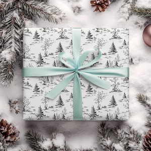 May include: A white gift box with a black and white winter forest print. The box is tied with a light blue ribbon.