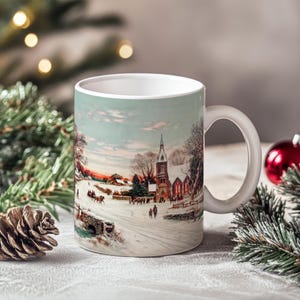 May include: White ceramic mug with a winter scene printed on it. The scene depicts a snowy village with a church in the background and people walking on a path.