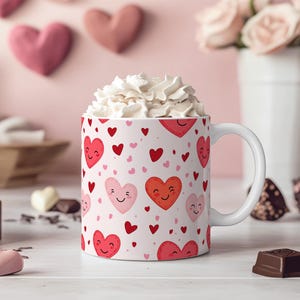 K&ouml;nnte beinhalten: Eine wei&szlig;e Keramiktasse mit einem Muster aus rosa und roten Herzen. Die Herzen haben l&auml;chelnde Gesichter. Die Tasse ist mit Schlagsahne gef&uuml;llt.