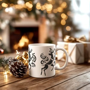 May include: White ceramic mug with a black silhouette design of two stylized reindeer. The mug has a handle and is sitting on a wooden table.
