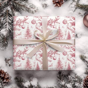 May include: A white gift box with a red and white floral pattern and a beige ribbon. The box is surrounded by pine branches and snow.