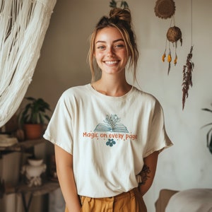May include: A white t-shirt with a graphic of an open book with flowers on top. The text "Magic on every page" is printed on the shirt.