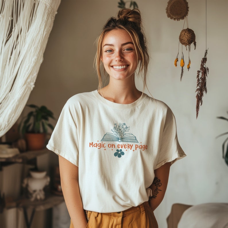 May include: A white t-shirt with a graphic of an open book with flowers on top. The text "Magic on every page" is printed on the shirt.