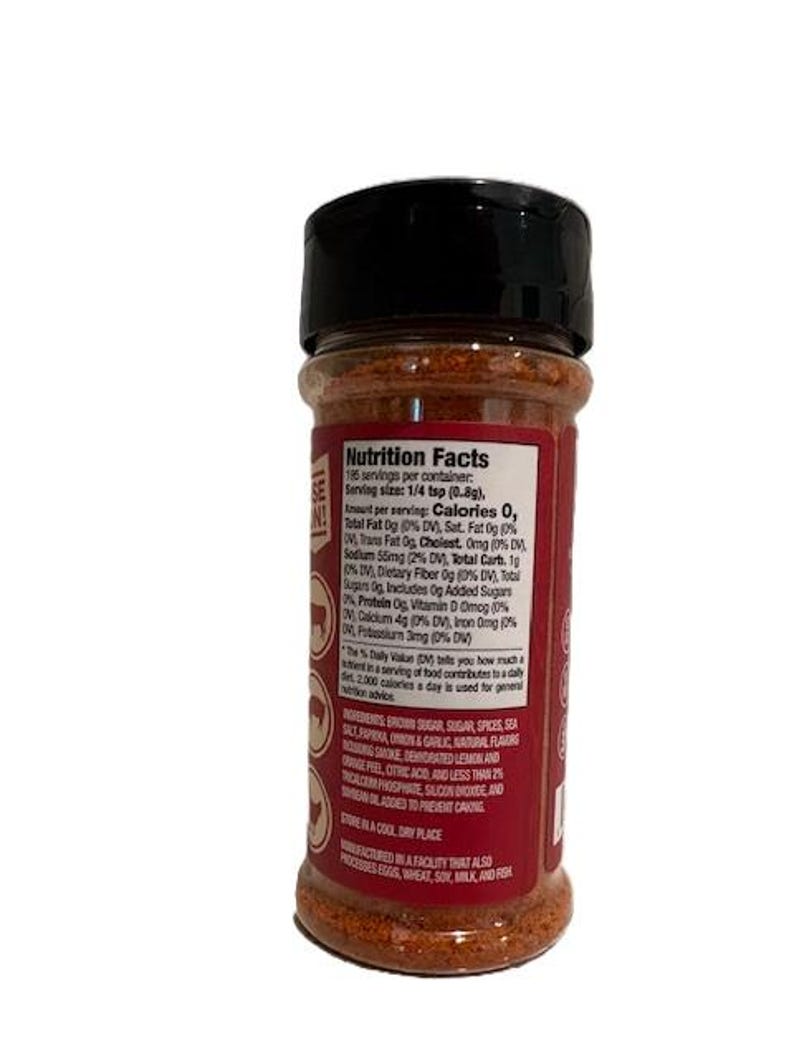 May include: A cylindrical spice container with a black lid and a red label. The label features white text detailing nutrition facts and ingredients. The container is filled with a brown spice blend, visible through the clear portion of the bottle.