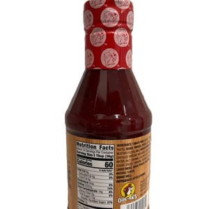 May include: A bottle of Buc-ee's brand sauce with a red cap featuring a repeating logo. The label includes nutrition facts and ingredients. The bottle is filled with a dark red sauce.