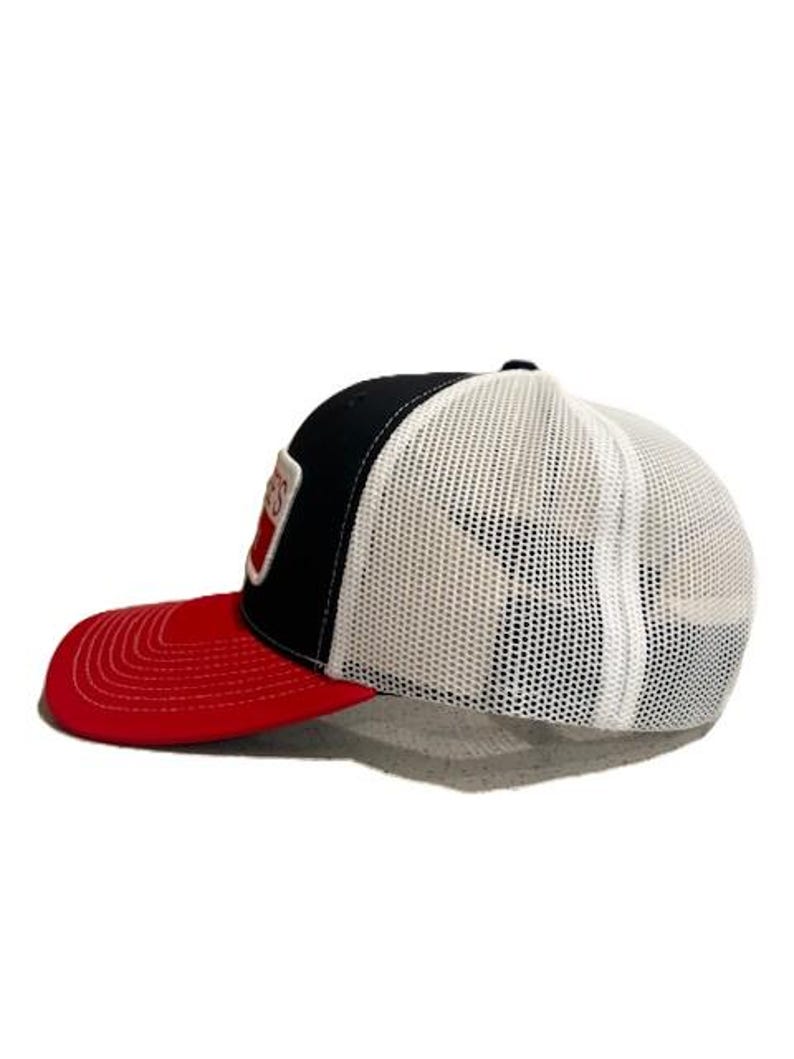 May include: A black, white, and red trucker hat with a mesh back and a curved brim. The front panel is black with a white and red patch. The brim is red.