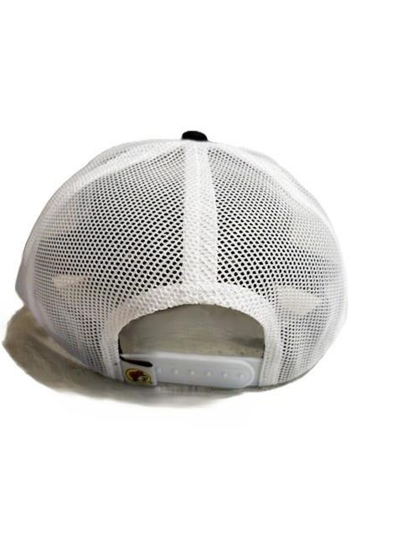 May include: White mesh-back baseball cap with a black button on top. The cap has a white adjustable snap closure. The back of the cap is made of a breathable mesh material.