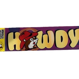 May include: A rectangular bumper sticker with the word "HOWDY!" in large yellow letters. The "O" in "HOWDY" features a cartoon beaver wearing a red cowboy hat. The background is purple with a rope design.