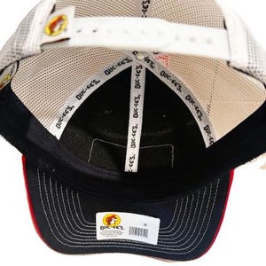 May include: A navy blue and red baseball cap with a white mesh back. The cap features the "Buc-ee's" logo and text on the inside and a white adjustable strap. The brim is navy blue with red trim.