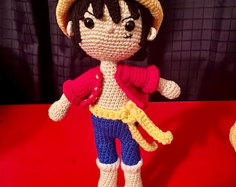 May include: Crocheted doll with a straw hat, red shirt, blue pants, and yellow belt. The doll is standing on a wooden base.