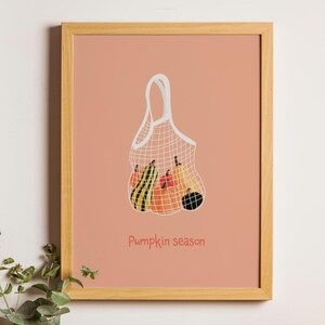 Peut inclure: Une illustration encadrée d'un sac en filet blanc rempli de citrouilles et de courges. Le fond est de couleur pêche clair et le texte "Pumpkin season" est écrit en rouge en bas de l'image.
