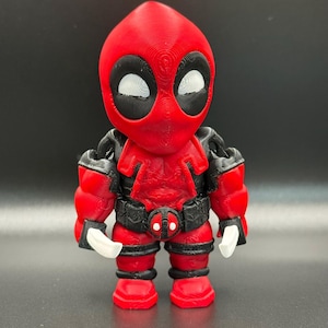 May include: A red and black 3D printed figurine of Deadpool with a muscular build. The figurine has a detailed design and white eyes.