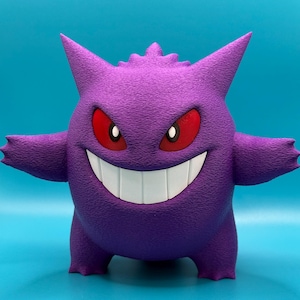 May include: A purple and white 3D printed figurine of a Ghost-type Pokémon, known as Gengar. The figurine has a wide grin with sharp teeth and red eyes.