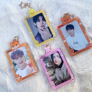 May include: Four colourful keychains featuring K-pop group Ateez members. Each keychain has a different member's photo and a cartoon animal design. The keychains are made of clear plastic and have a metal ring for attaching to keys.