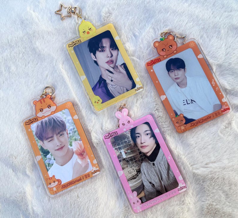 May include: Four colourful keychains featuring K-pop group Ateez members. Each keychain has a different member's photo and a cartoon animal design. The keychains are made of clear plastic and have a metal ring for attaching to keys.