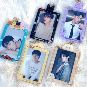 May include: Five colourful photo card holders with clear plastic frames and gold accents. Each holder features a cartoon animal and the name "Ateez" printed on the bottom. The holders are decorated with different cartoon animals, including a black cat, a purple cat, a yellow puppy, and a white puppy. The photo cards feature different members of the K-pop group Ateez.
