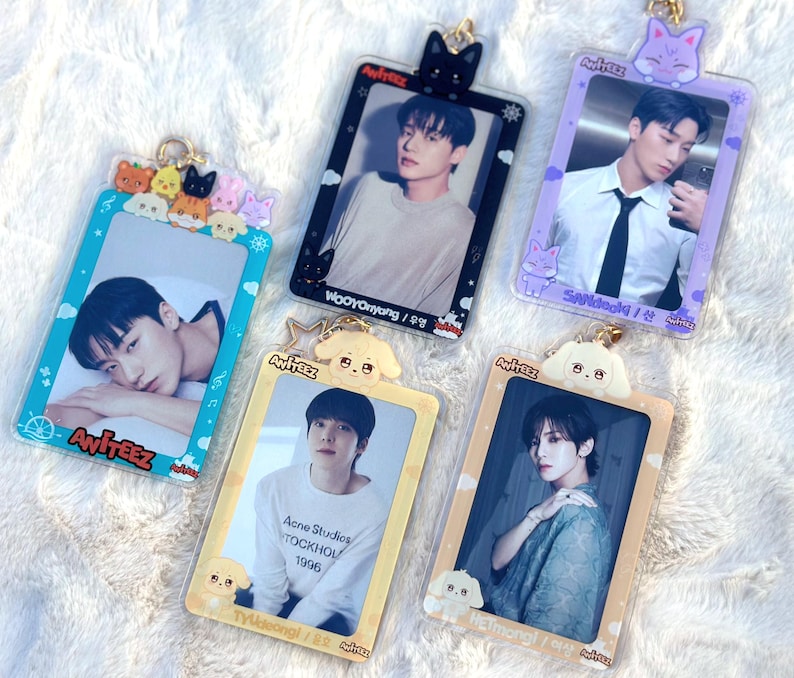 May include: Five colourful photo card holders with clear plastic frames and gold accents. Each holder features a cartoon animal and the name "Ateez" printed on the bottom. The holders are decorated with different cartoon animals, including a black cat, a purple cat, a yellow puppy, and a white puppy. The photo cards feature different members of the K-pop group Ateez.