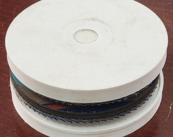 May include: A white plastic container with a stack of sanding discs inside. The discs are black and blue with a serrated edge.