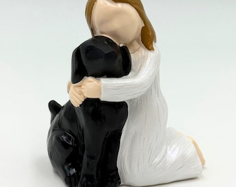 May include: A figurine of a girl in a white dress kneeling and hugging a black dog. The girl has light brown hair and a neutral skin tone. The dog is a solid black color, and the figurine is set against a white background.