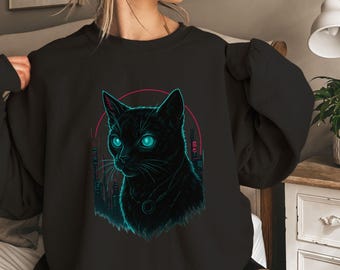 May include: Black sweatshirt featuring a stylized cat portrait with glowing teal eyes and a matching teal outline. The cat is set against a pink circle with a cityscape backdrop. The design is a graphic illustration.