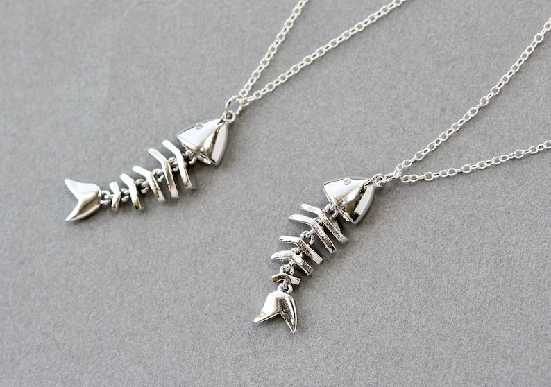 Puede incluir: Dos collares de plata con colgantes de espinas de pescado. Los colgantes son detallados y realistas, con un acabado plateado.