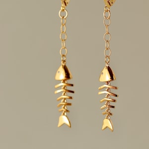 Op de afbeelding: Gouden visgraat oorhangers met een delicate ketting. De oorbellen hebben een eenvoudig, minimalistisch ontwerp.