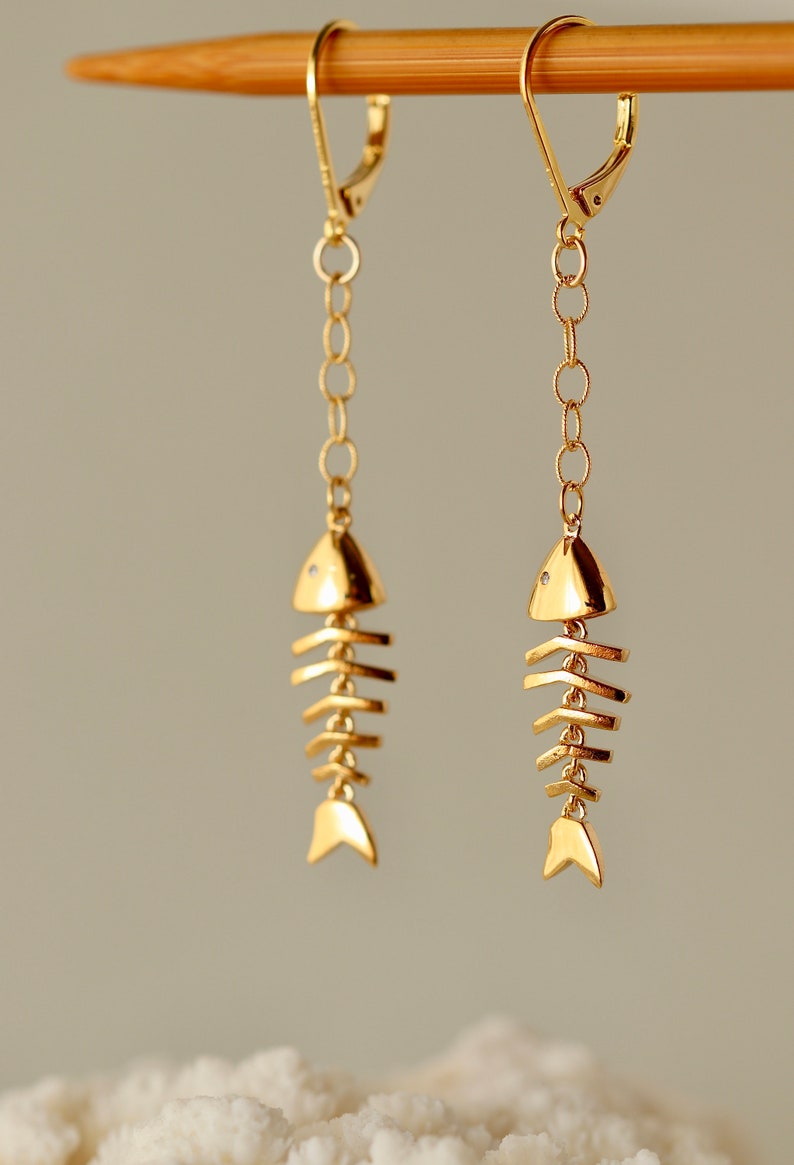 Op de afbeelding: Gouden visgraat oorhangers met een delicate ketting. De oorbellen hebben een eenvoudig, minimalistisch ontwerp.