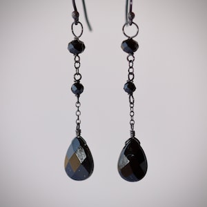 May include: Black dangle earrings with a teardrop-shaped black crystal and black beads.