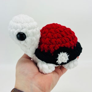 May include: A crocheted turtle plush toy with a red, black, and white shell. The shell has a white star in the center.