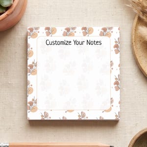 May include: A square notepad featuring a white centre bordered by a pattern of brown and tan botanical illustrations and circles. The text "Customize Your Notes" is printed in black at the top centre of the notepad against a light background.