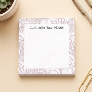 May include: A square notepad with a light purple seashell pattern border and the text Customize Your Notes printed at the top. The notepad is accompanied by three pens with light-colored barrels and a single gold-toned metal paper clip.