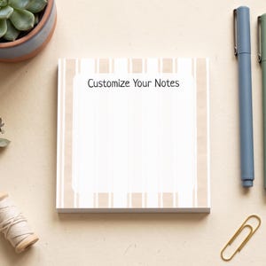 May include: A square notepad with a white centre and beige vertical stripes, featuring the text "Customize Your Notes" at the top. The notepad is accompanied by three pens in blue, green, and yellow, a spool of twine, a paperclip, and a succulent.