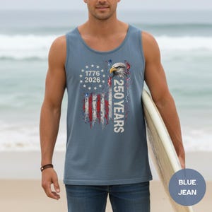The image showcases a Comfort Colors 9360 Midweight Tank Top featuring a patriotic design. The shirt prominently displays an eagle, the years "1776" and "2026," and a distressed American flag motif. This stylish T-shirt is available in nine colors and sizes ranging from S-3XL, making it a perfect choice for celebrating American pride during Independence Day, family gatherings, or casual outings. The heavyweight fabric ensures comfort and durability, making it an ideal addition to any wardrobe.