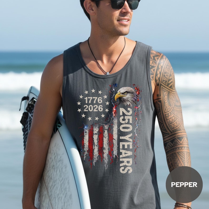 The image showcases a Comfort Colors 9360 Midweight Tank Top featuring a patriotic design. The shirt prominently displays an eagle, the years "1776" and "2026," and a distressed American flag motif. This stylish T-shirt is available in nine colors and sizes ranging from S-3XL, making it a perfect choice for celebrating American pride during Independence Day, family gatherings, or casual outings. The heavyweight fabric ensures comfort and durability, making it an ideal addition to any wardrobe.