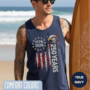 The image showcases a Comfort Colors 9360 Midweight Tank Top featuring a patriotic design. The shirt prominently displays an eagle, the years "1776" and "2026," and a distressed American flag motif. This stylish T-shirt is available in nine colors and sizes ranging from S-3XL, making it a perfect choice for celebrating American pride during Independence Day, family gatherings, or casual outings. The heavyweight fabric ensures comfort and durability, making it an ideal addition to any wardrobe.