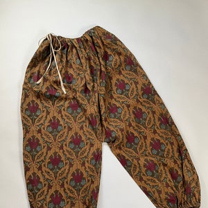 May include: Brown pants with a floral pattern in shades of red, green, and gold. The pants have an elastic waistband and a drawstring.