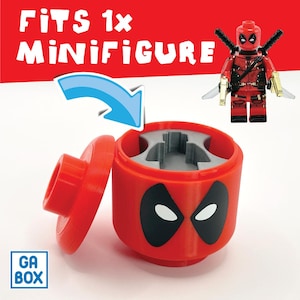 Puede incluir: Contenedor de almacenamiento rojo con un diseño de cara de Deadpool, abierto con la tapa al lado. El texto "FITS 1x MINIFIGURE" está en la parte superior. Se muestra una minifigura de Deadpool. El contenedor tiene un inserto de espuma gris.