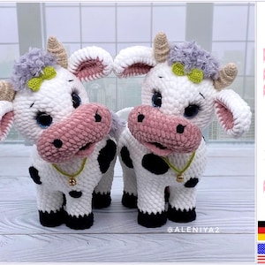 以下が含まれることがあります： 白い毛並み、黒い斑点、ピンクの鼻、緑のリボンが付いた、かぎ針編みで作られた牛のぬいぐるみが2体。ぬいぐるみは首に鈴が付いており、白い木製の表面の上に立っています。画像の右上に「Pattern PDF」というテキストがあります。