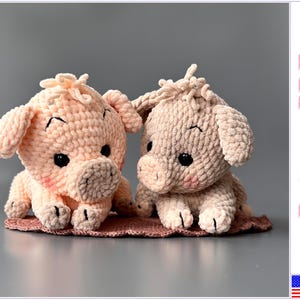May include: Two crocheted plush pig toys made from soft, textured yarn. The left pig is light pink, and the right pig is a muted beige. Both feature black plastic eyes, small ears, tufts of hair on top, and pink blush on their cheeks. Text reads Pattern PDF.