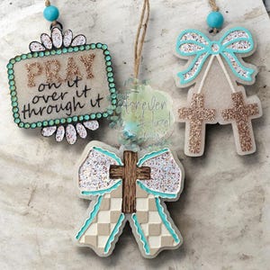 May include: Three hanging ornaments with turquoise beads and twine. One is a rectangular sign with glittery text reading PRAY on it over it through it. Another features a turquoise bow with two glittery crosses. The third is a bow with a cross.