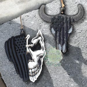 May include: Two decorative car air fresheners. One is a skull with an American flag design, the other is a bull skull with an American flag design. Both are black and white and have a string for hanging.